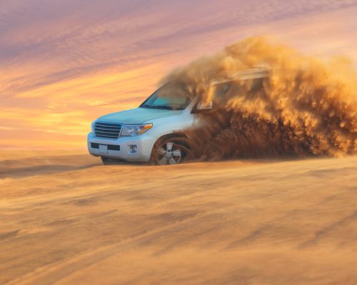 Off-road adventure with SUV in Arabian Desert at sunset. Offroad vehicle bashing through sand dunes in Dubai desert.